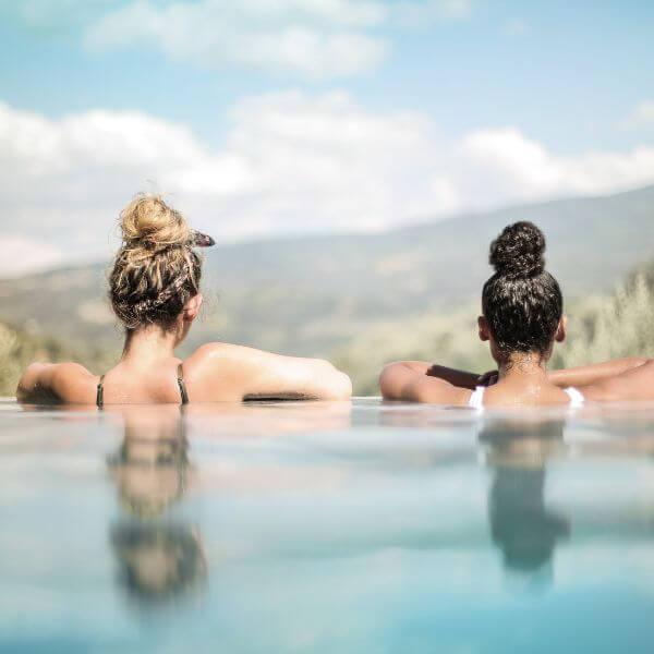 deux femmes de dos dans une piscine avec les montagnes en arrière plan